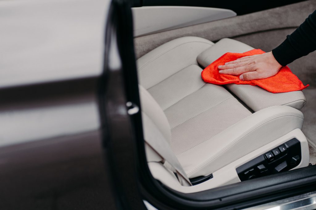 Faceless man cleans car interior uses cloth to wipe leather seat