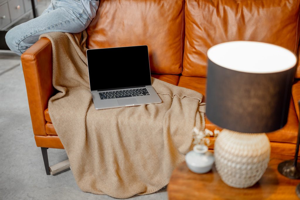 Open laptop lying on foxy leather sofa at home